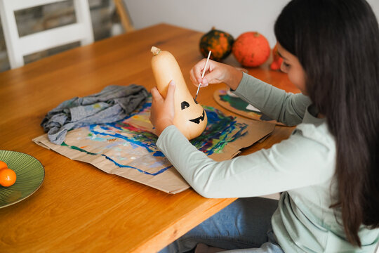 Female kid painting a pumpkin for an halloween party fest - Holidays and art concept - UGC content - Main focus on right hand
