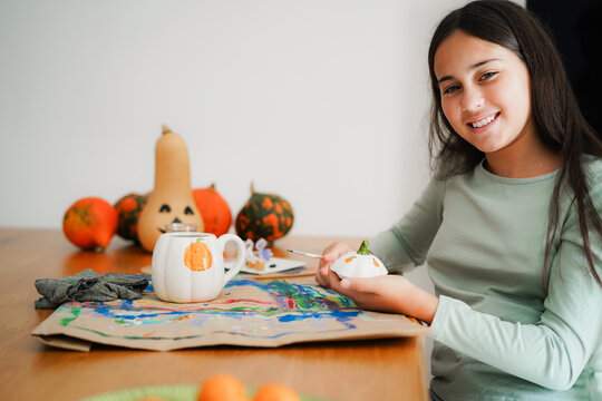Female kid painting a pumpkin on a cup for an halloween party fest - Holidays and art concept - Main focus on face - UGC content