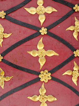 Golden floral ornaments and curved black iron bands decorate the red surface of a historic gate. The close-up shows traditional craftsmanship and a decorative geometric pattern.