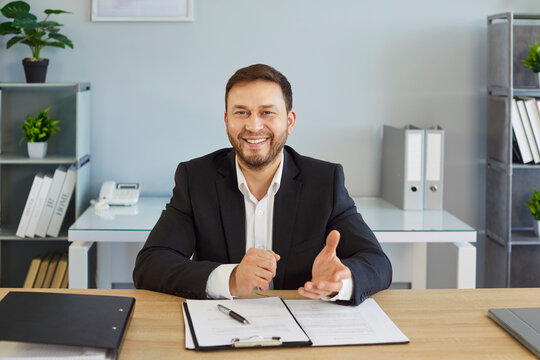 Businessman in office during video call sitting at desk. Employee smiles and gestures as skilled presenter, sharing webinar tips and remote communication online during conference. Technology concept