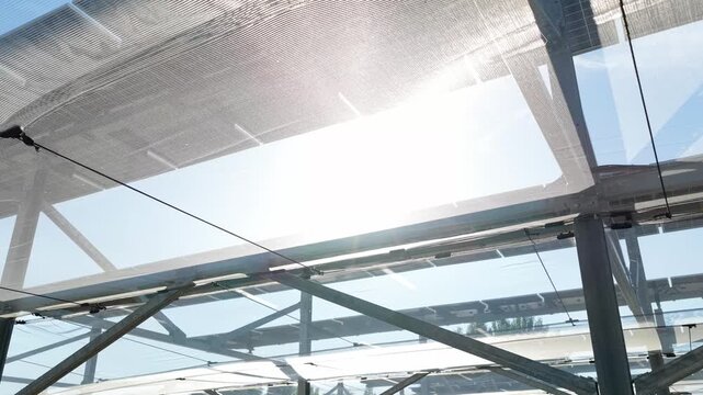 Aerial view of a modern agrivoltaic solar panel structure with metal framing and translucent panels under bright sunlight in Faenza, Emilia-Romagna, Italy.