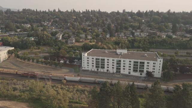 Freight train along Interstate 84 in Hood River, Oregon, with residential neighborhoods, trees, and hazy summer conditions in the Columbia River Gorge.