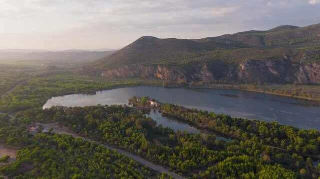 Kaiafas lake nestled between steep limestone cliffs of Mount Lapithas and pine forest at sunset, tiny Aghia Ekaterini islet at centre, Zacharo, Ilia, Drone shot