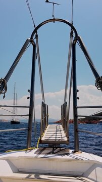 Vertical view from the bow of moving cruise ship looking towards the gangway the open sea, a distant yacht and a mountainous Mediterranean coastline under blue, slightly cloudy sky. Sardinia, Italy.