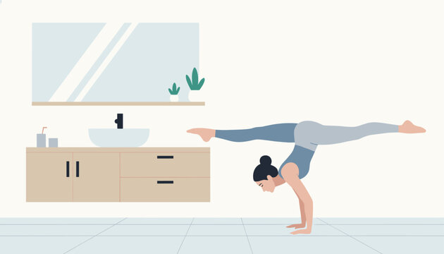 Athletic young woman practicing an impressive handstand split yoga pose inside a modern bathroom next to a wooden vanity.