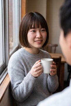 Holding a mug, a Japanese woman smiles at her companion