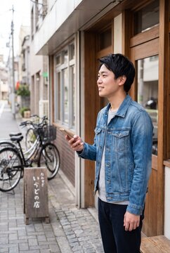 Smiling Japanese man with smartphone by shopfront