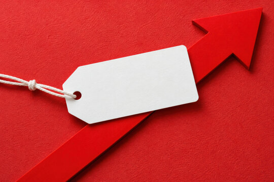 Blank white price tag tied to a red upward arrow on a red background, symbolizing rising prices, sales growth, and business success.