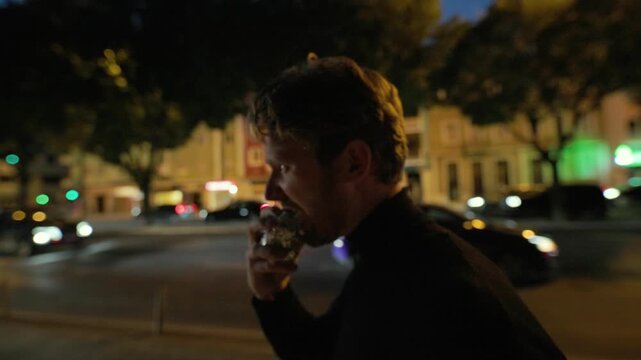 Man eating shawarma wrap on city street at night