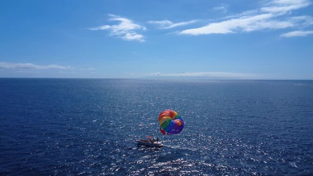 Vista a&eacute;rea de un parasailing multicolor arrastrado por una lancha r&aacute;pida sobre el mar azul brillante frente a Costa Adeje, Tenerife