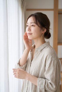 Beside a curtain, a Japanese woman touches her cheek