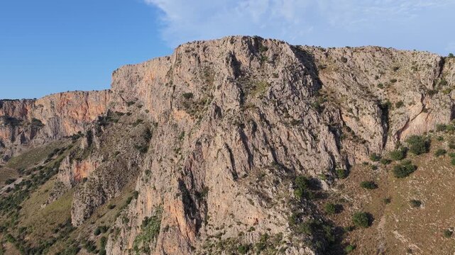 Aerial view of rugged limestone cliffs with sparse vegetation and rocky terrain in Terrasini, Sicily, Italy.