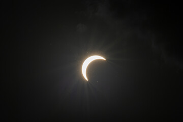 Partial solar eclipse captured as the Moon passes in front of the Sun, creating a striking crescent shape against the dark sky. An astronomical event photographed during daylight. © KjLOWRYPHOTOGRAPHY