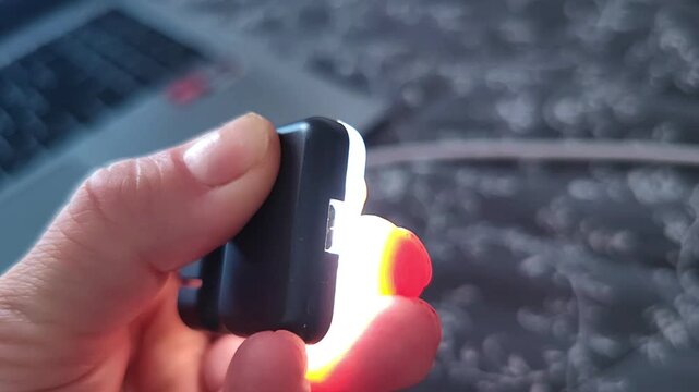 Hand switches on a compact LED light for a phone, showing the illuminated device and its portable design, mobile photography equipment, content creation accessory.