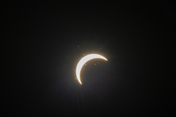 Partial solar eclipse captured as the Moon passes in front of the Sun, creating a striking crescent shape against the dark sky. An astronomical event photographed during daylight. © KjLOWRYPHOTOGRAPHY