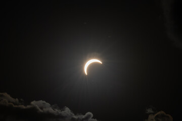 Partial solar eclipse captured as the Moon passes in front of the Sun, creating a striking crescent shape against the dark sky. An astronomical event photographed during daylight. © KjLOWRYPHOTOGRAPHY