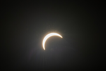 Partial solar eclipse captured as the Moon passes in front of the Sun, creating a striking crescent shape against the dark sky. An astronomical event photographed during daylight. © KjLOWRYPHOTOGRAPHY