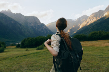 Obraz premium Woman with a backpack gazes over a mountain valley, exploring nature and outdoor life. Bright sky, green fields, distant peaks create a calm, adventurous mood for travel lifestyle.
