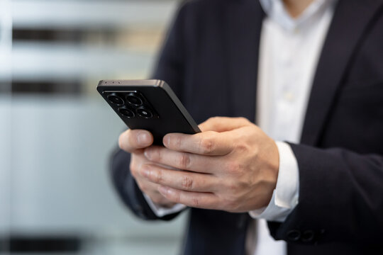 Businessman using a smartphone for digital communication and corporate networking tasks. Professional man in a suit holding a mobile phone to manage business operations in a modern office environment.