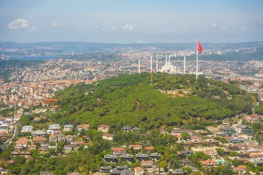 Aerial view of a green hill with Turkish flag and cityscape in the background, showcasing residential areas and urban development in Istanbul, Turkey 