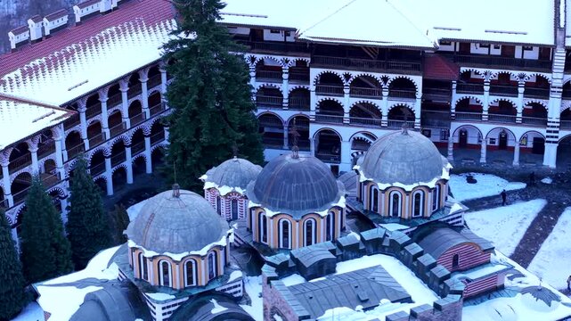 Aerial view of the historic Rila Monastery with its iconic domes and striped architecture covered in snow in Rilski manastir, Kyustendil, Bulgaria.