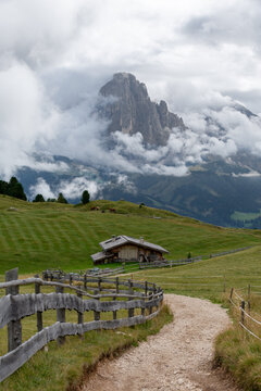 Sankt Ulrich, Italy - August 25, 2026: Mountain hut on alpine pasture below cloud-covered peak