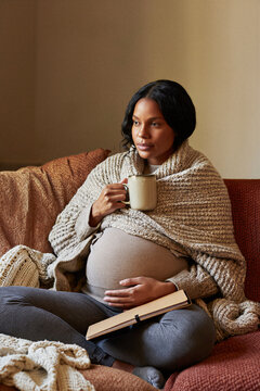 Pregnant woman journaling with a warm mug on the couch