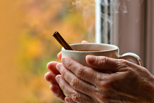 Hands wrapped around a warm cider mug with steam rising