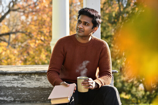 Young man in wool sweater reading on autumn porch steps