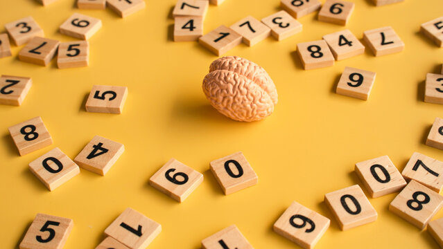 Human Brain Model Surrounded by Wooden Number Tiles on Bright Yellow Background