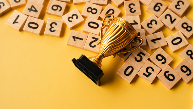 Golden trophy cup on wooden number tiles over yellow background representing achievement and excellence in mathematics