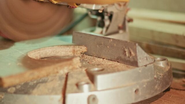 Close-up of a craftsman using an electric miter saw to cut a wide wooden board in a workshop. Flying sawdust and precise blade action for carpentry and construction projects