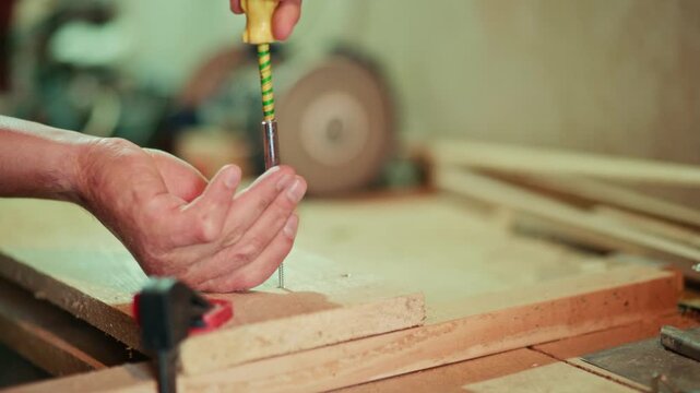 Close-up of a craftsman using a manual screwdriver to fasten a screw into a wooden plank in a workshop. Authentic handmade DIY woodworking footage for craft and maker projects