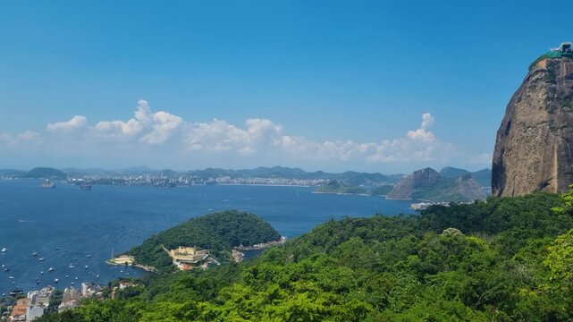 Breathtaking view from Morro da Urca in Rio de Janeiro, overlooking Guanabara Bay and the iconic Sugarloaf Mountain, surrounded by lush tropical vegetation and blue skies