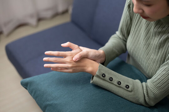 A young woman is experiencing pain in her hands and fingers and is trying to relieve the discomfort by massaging them gently.