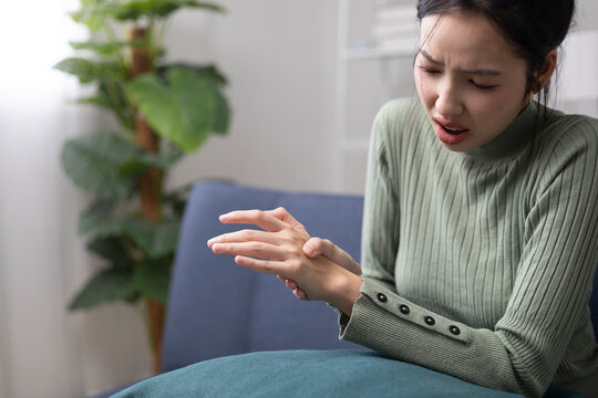 A young woman is experiencing pain in her hands and fingers and is trying to relieve the discomfort by massaging them gently.