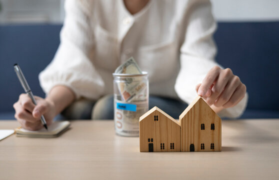 A young woman is sitting and shopping for a house using money she saved in a piggy bank, while noting down expenses and keeping track of her finances.