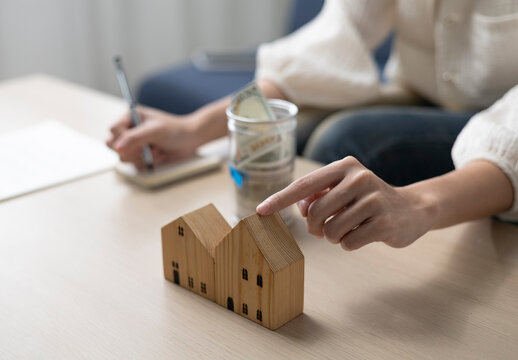 A young woman is sitting and shopping for a house using money she saved in a piggy bank, while noting down expenses and keeping track of her finances.