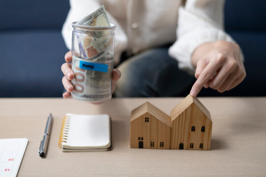 A young woman is sitting and shopping for a house using money she saved in a piggy bank, while noting down expenses and keeping track of her finances.