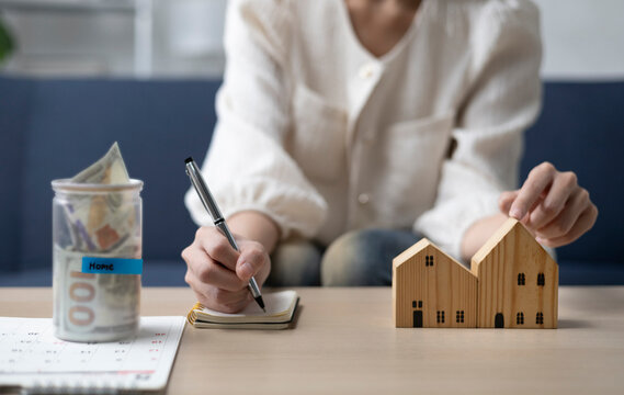 A young woman is sitting and shopping for a house using money she saved in a piggy bank, while noting down expenses and keeping track of her finances.