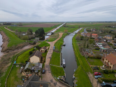 Aerial view looking upstream from Salters Lode Lock in Norfolk, England, showing narrowboats, waterways and drainage channels stretching across the flat Fenland landscape.