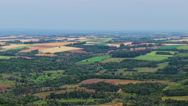 High angle drone view tracking right across green and yellow agricultural fields and rolling vegetated hills stretching until the horizon.