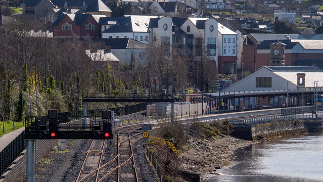 View from Derry's Peace Bridge across railway tracks curving into Derry railway station beside the River Foyle, with the city's buildings rising in the background.