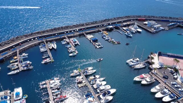 Dron vuela a lo largo del rompeolas de Puerto Col&oacute;n con filas de barcos amarrados y lanchas saliendo del puerto, Costa Adeje, Tenerife, Espa&ntilde;a