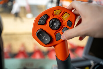 Operator hand holding multifunctional orange joystick controller with push buttons inside modern agricultural combine harvester cabin. © Marina