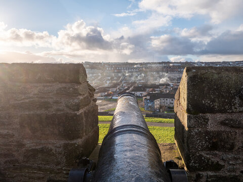View of the Bogside, Derry in the North of Ireland, with a cannon poking through the historic walls, offering a panoramic view of the town and surrounding hills under a partly cloudy sky.