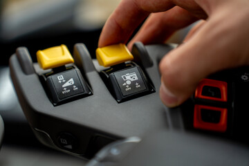 Close-up of operator hand toggling yellow hydraulic control lever switch on joystick console inside modern agricultural tractor cabin. © Marina