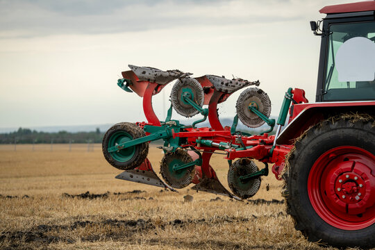 Modern agricultural tractor with lifted reversible plow implement preparing for soil cultivation on dry stubble field.