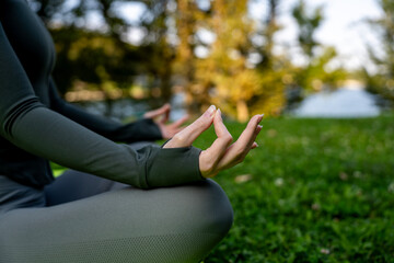 Obraz premium Woman sitting in lotus position on fitness mat practicing yoga and meditation with hand in gyan mudra outdoors on green grass in park.