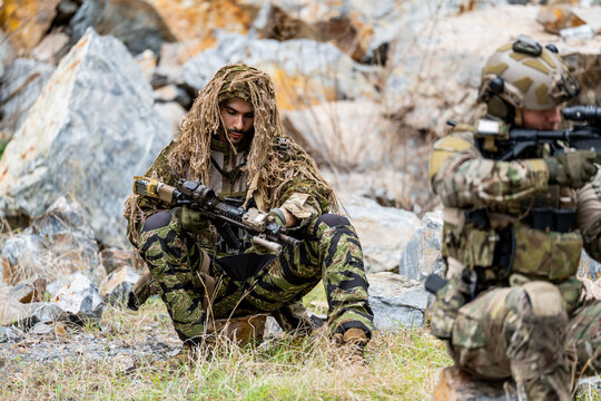 Soldiers in camouflage gear resting during a training exercise in a rocky outdoor area